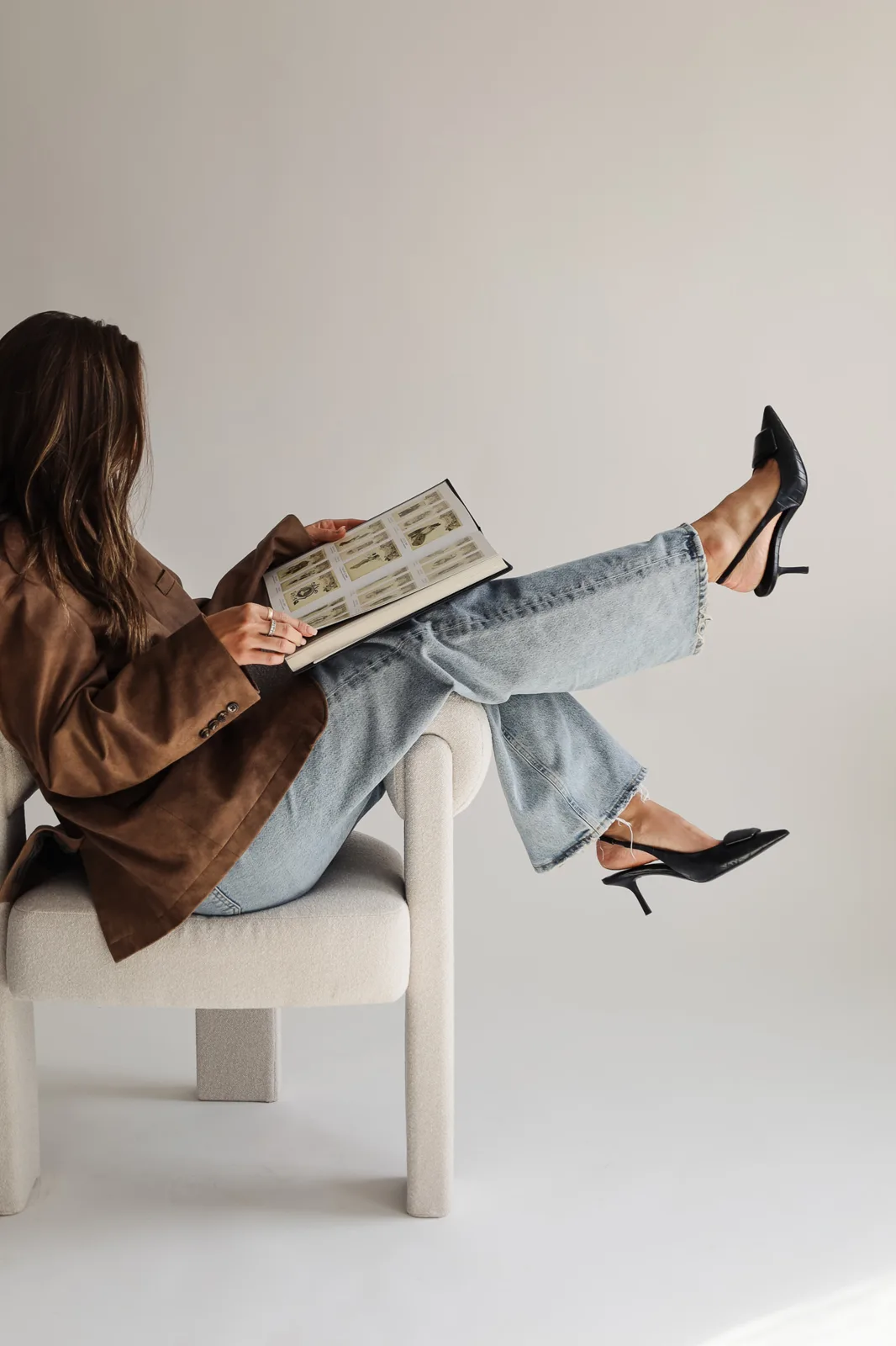 A woman in a brown blazer and jeans reading a magazine with her feet up